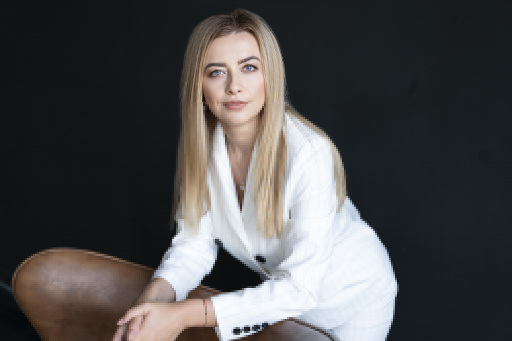 Дівчина в білому діловому костюмі стоїть спершись на спинку крісла.