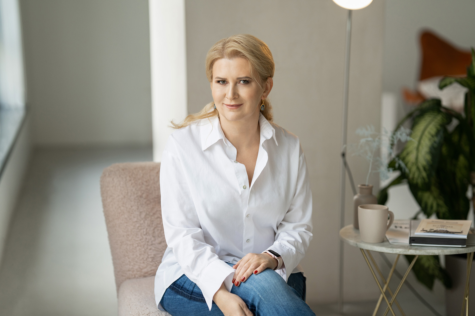 Дівчина в біла кофтинка і джинси сидить на стільці біля кави