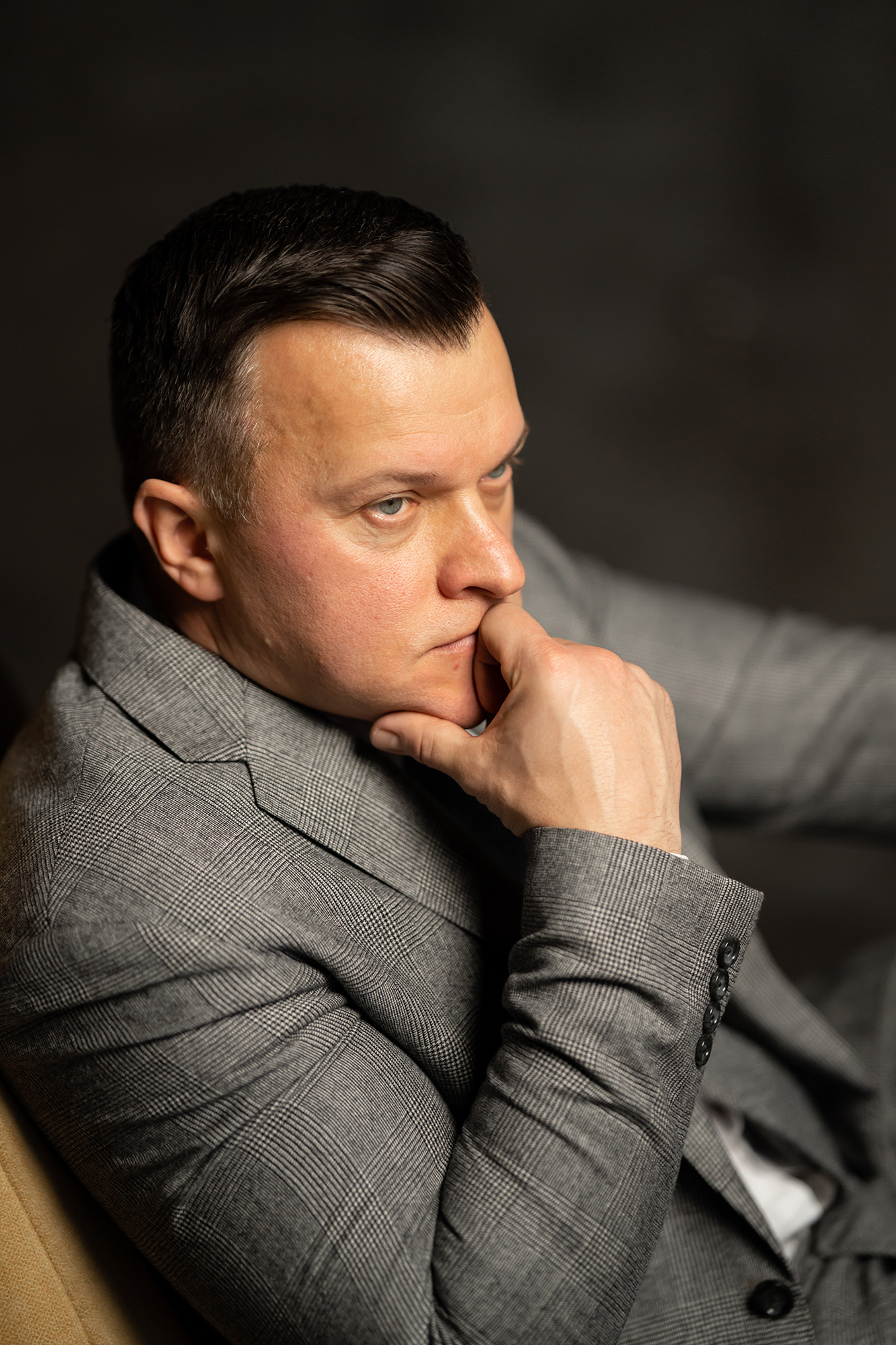 Хлопець у сірому піджаку задумливо підтримує себе за підборіддя