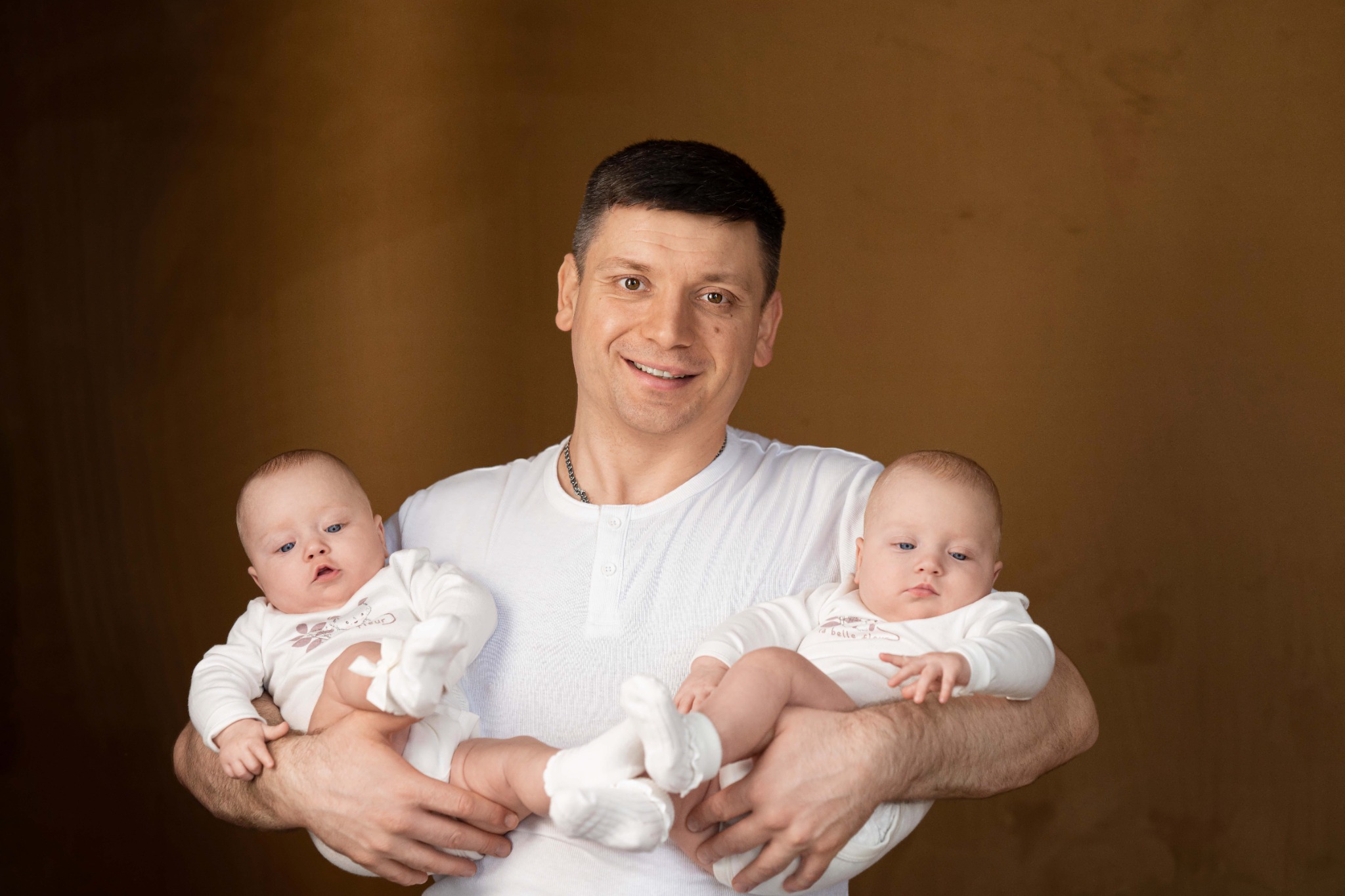 Тато з двійнятами на руках на фоні кавової стіни
