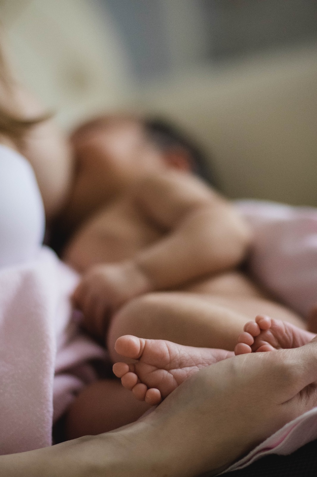 Крихітні ніжки немовляти в руках матері-годувальниці в пледі.