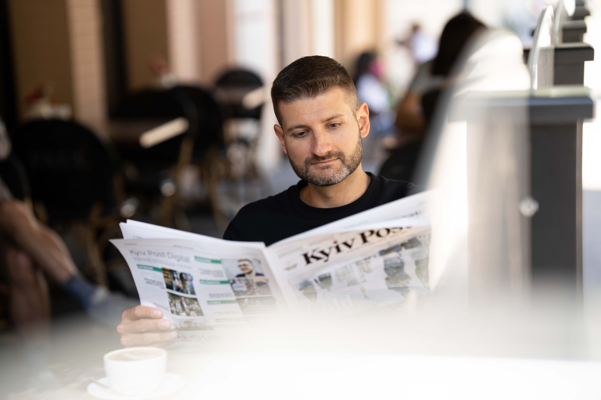 Чоловік у кафе читає газету Kyiv Post за чашкою кави
