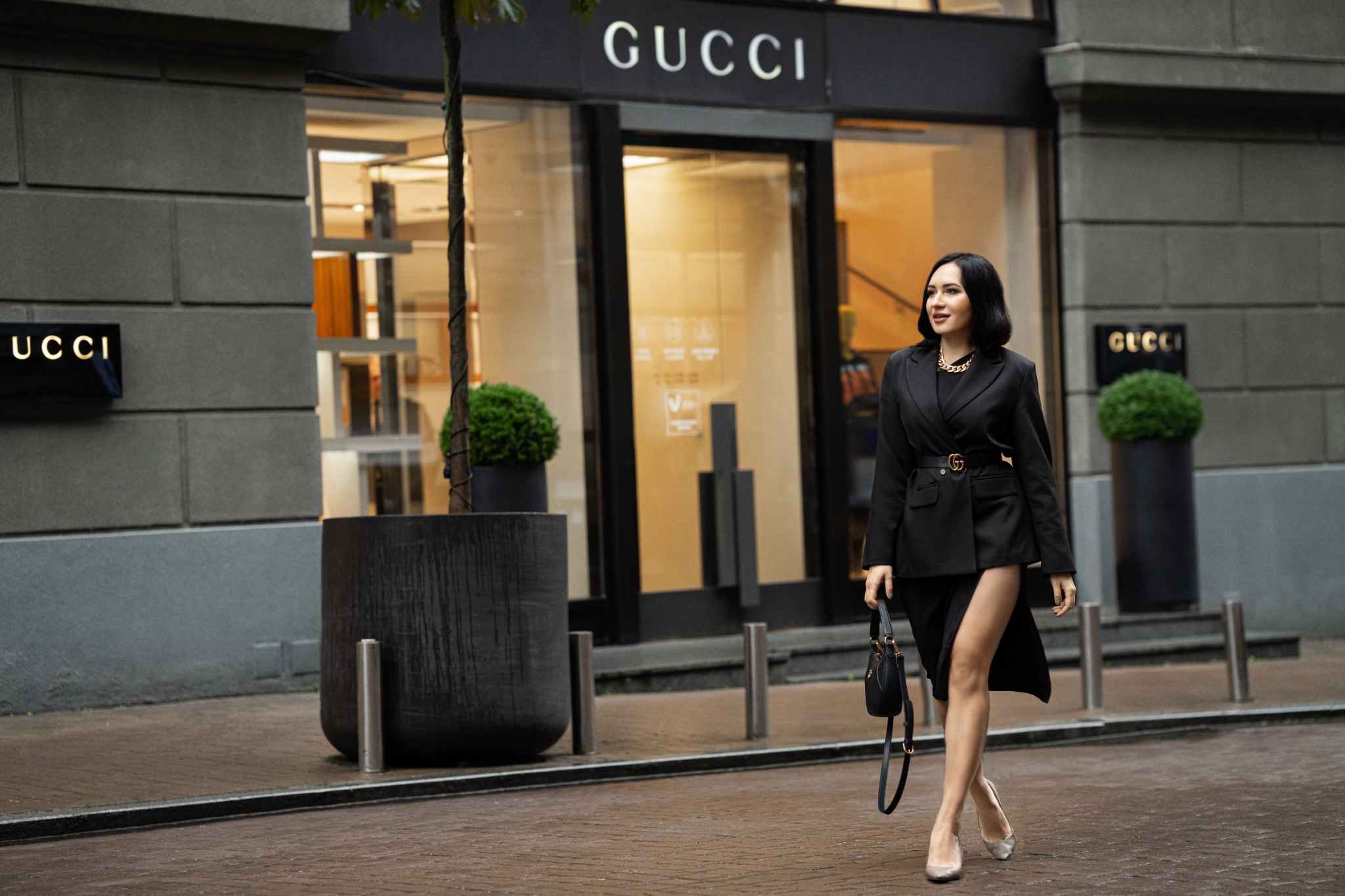 Стильна жінка в чорному жакеті йде повз бутік Gucci