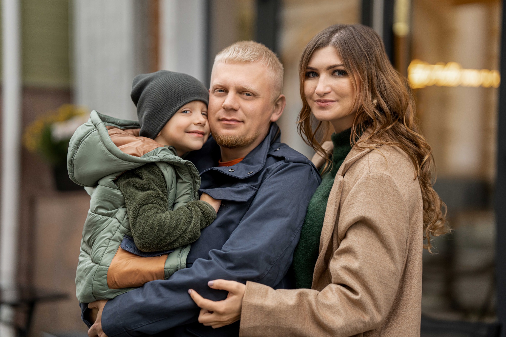 Маленький син притиснувся до тата та мами, а родина обіймається у місті.