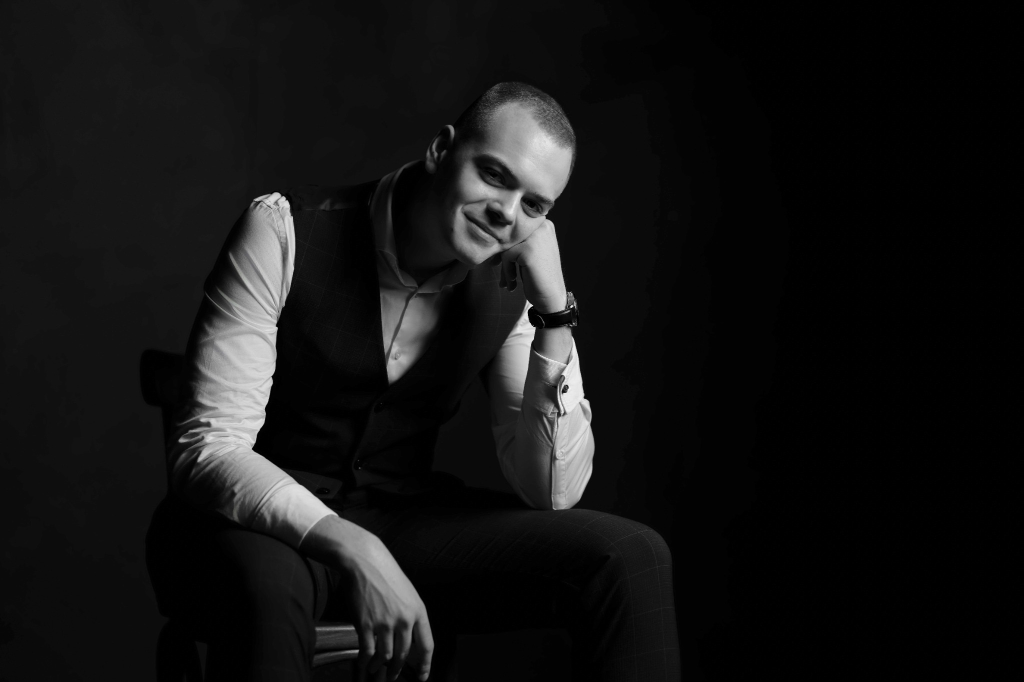 Молодий чоловік у жилеті постановки, сидячи на стільці в студії.