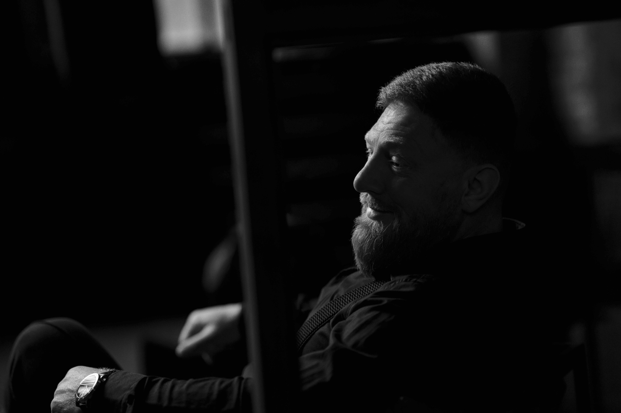 Чоловік з бородою у профіль сидить у затемненій фотостудії