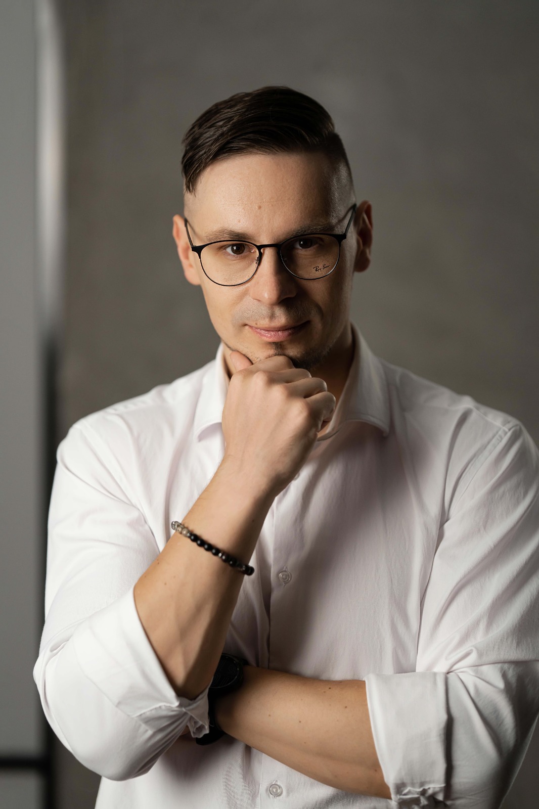 Молодий фахівець у білій сорочці та окулярах позує біля стіни, передаючи впевненість та професіоналізм працівника IT-компанії або digital-агентства.