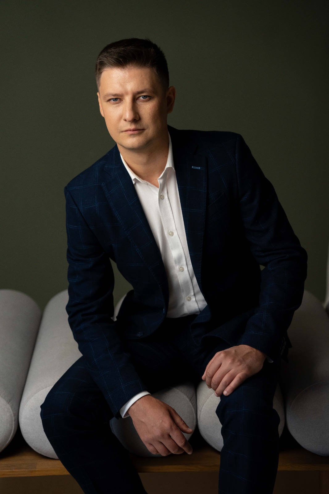 Чоловік у блакитному костюмі і біла сорочка позують сидячи в офісній зоні.