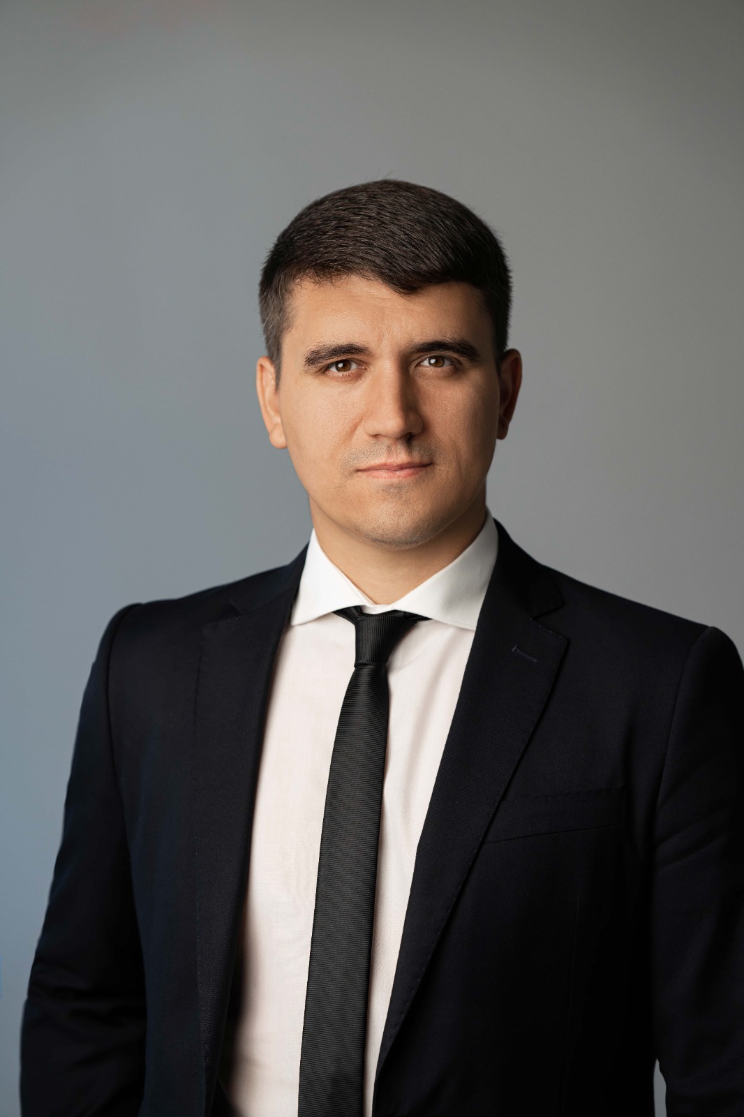 Чоловік у суворому чорному костюмі та білій сорочці постановки на сірий фон, погляд впевнений